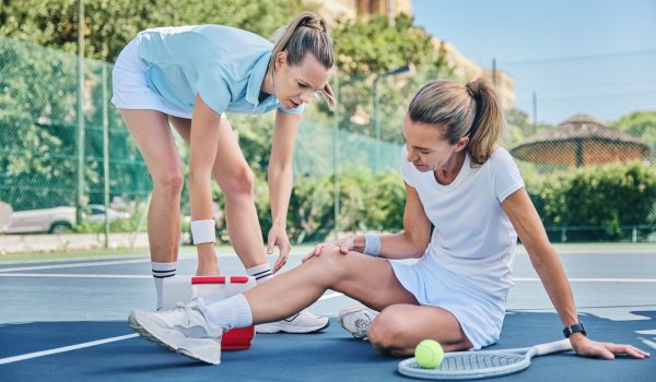 Tennis, medic with first aid and woman with knee pain, torn muscle or inflammation on court while training. Female coach, mentor or help athlete with strain, tender or broken leg with outdoor fitness.